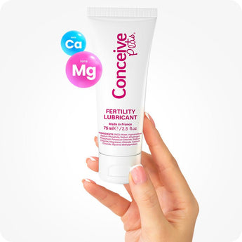 Conceive Plus Fertility Lubricant (2.5 fl. oz) tube held upright by a woman's hand with neatly manicured nails, highlighting product's calcium and magnesium ion content in floating icons, with front-facing label and white background enhancing clinical and personal care aesthetic.
